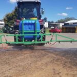 AG king boom spray attached to the back end of a green tractor carrying a blue tank