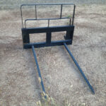 Empty two-tine bale spear sitting on level dirt surface