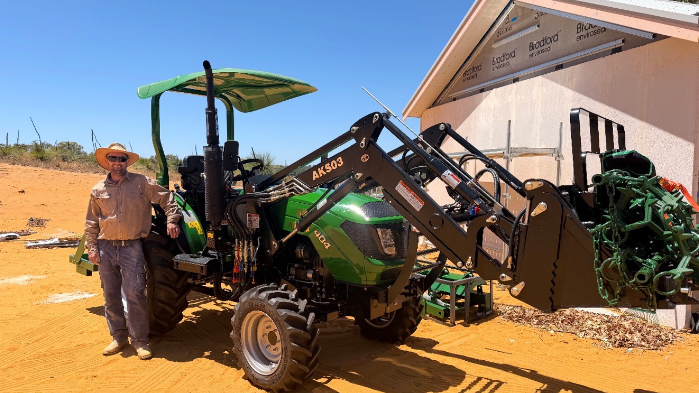 Outback famer stands next to his AgKing AK404 tractor with front-end loader full of metal 