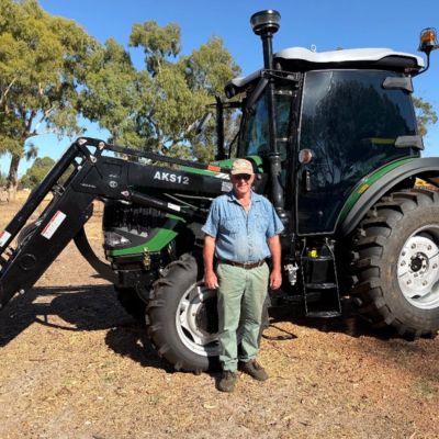Farmer stands in front of an Enfly AKS12 tractor parked outside with gumtrees in the background