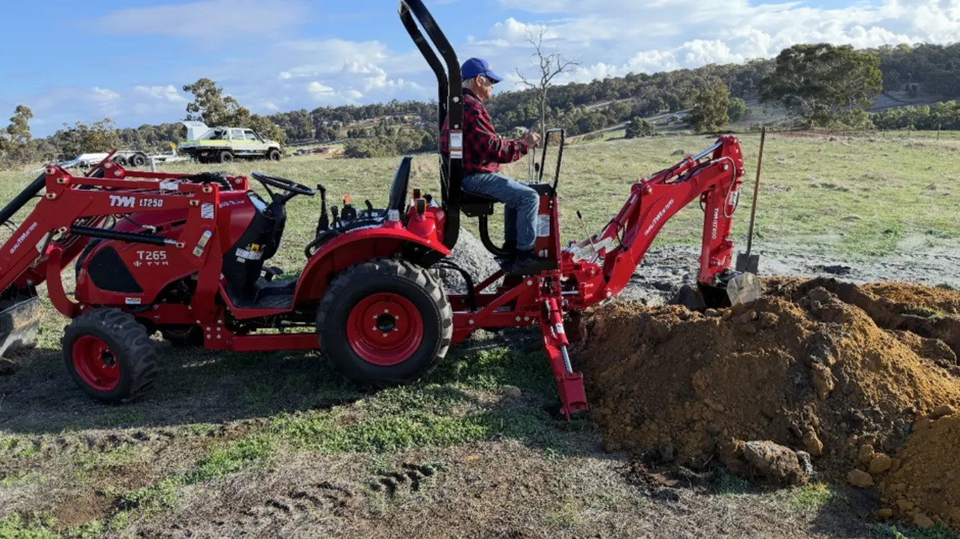 TYM T265 compact tractor with backhoe attachment digging soil on a rural property