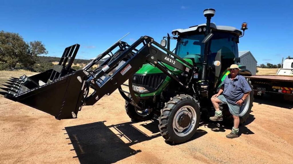 Green Enfly tractor with front loader bucket parked on a farm property, with a man leaning against the wheel
