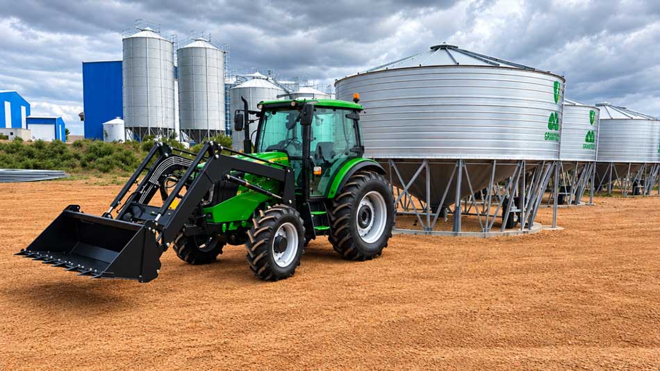 Engine, transmission and power Green tractor fitted with a front-end loader bucket, parked outside grain storage silos on a farm.